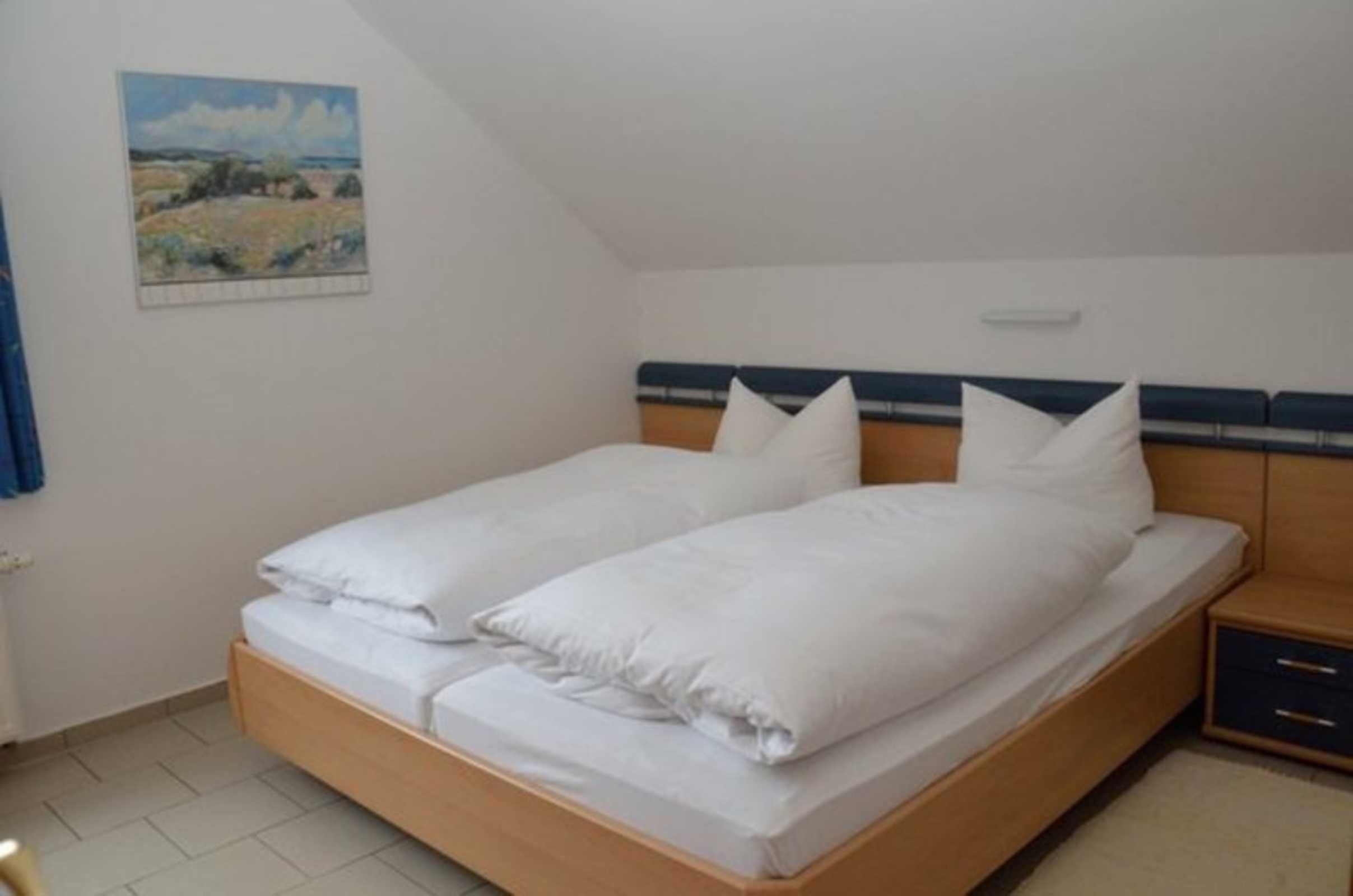 A single bed with white bedding, a headboard with a blue stripe, a nightstand with a drawer, and a painting on the wall.