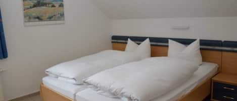 A single bed with white bedding, a headboard with a blue stripe, a nightstand with a drawer, and a painting on the wall.