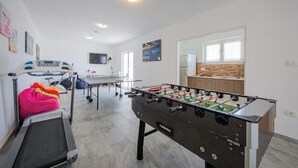 A modern living room with a foosball table, exercise equipment, and a kitchen area. - Lovely home in Podpican (Podpican)