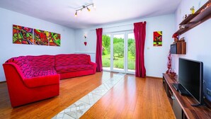 A modern living room with a red sofa, a flat-screen TV, and large windows with red curtains. - Lovely home in Podpican (Podpican)
