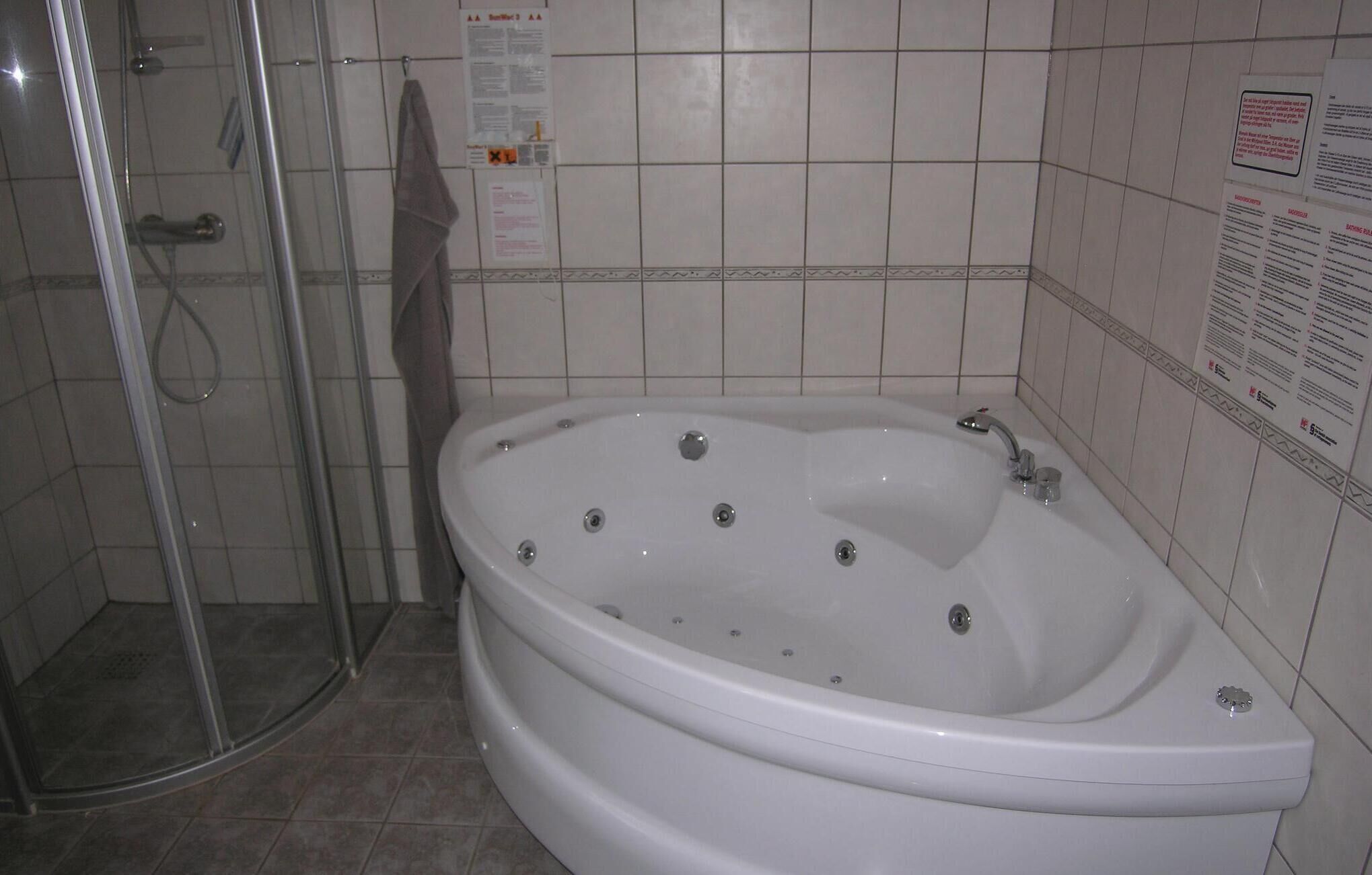 Un baño con una bañera grande, cabina de ducha de vidrio y paredes revestidas de azulejos.