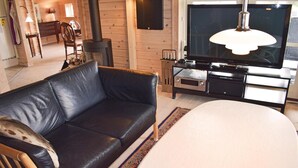 A cozy living room with a black leather sofa, a wooden TV stand, a fireplace, and a large TV. - Amazing home in Tranekær with sauna (Tranekær)
