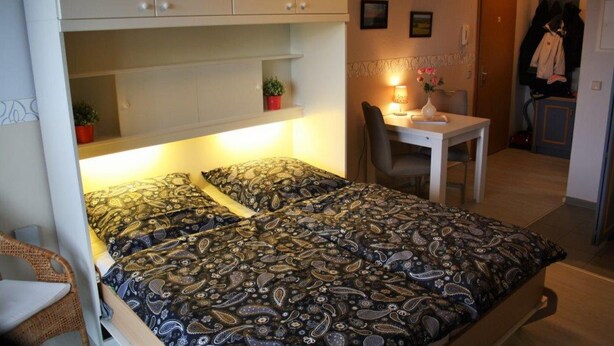 Een kleine slaapkamer met een bed, bureau en stoel.