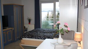 Een slaapkamer met een bed, een televisie, een bureau met lamp, een vaas met bloemen en een raam met uitzicht op het landschap.