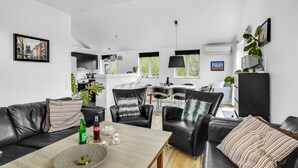 En moderne stue med en sort lædersofa, et spisebord med stole og et køkken i baggrunden.