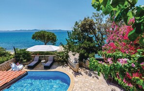 Un área de piscina con vista al mar, sillas de descanso y una sombrilla blanca.