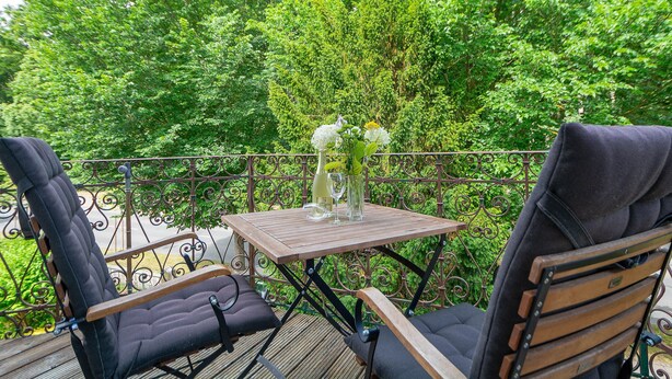 Eine Holzterrasse mit zwei schwarzen Liegestühlen und einem kleinen Tisch mit einem Blumenstrauß.