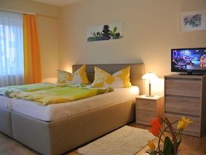 A bedroom with a bed, bedside table, lamp, TV, and a painting on the wall.