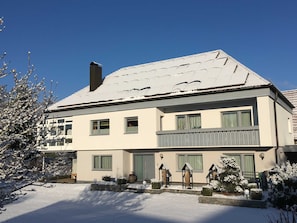 A two-story house with a snow-covered roof, multiple windows, and a balcony.