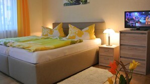 A bedroom with a bed, a nightstand, a TV, a lamp, and a painting on the wall.