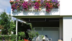 A two-story building with a balcony filled with colorful flowers, a garage door, and potted plants in the front yard.