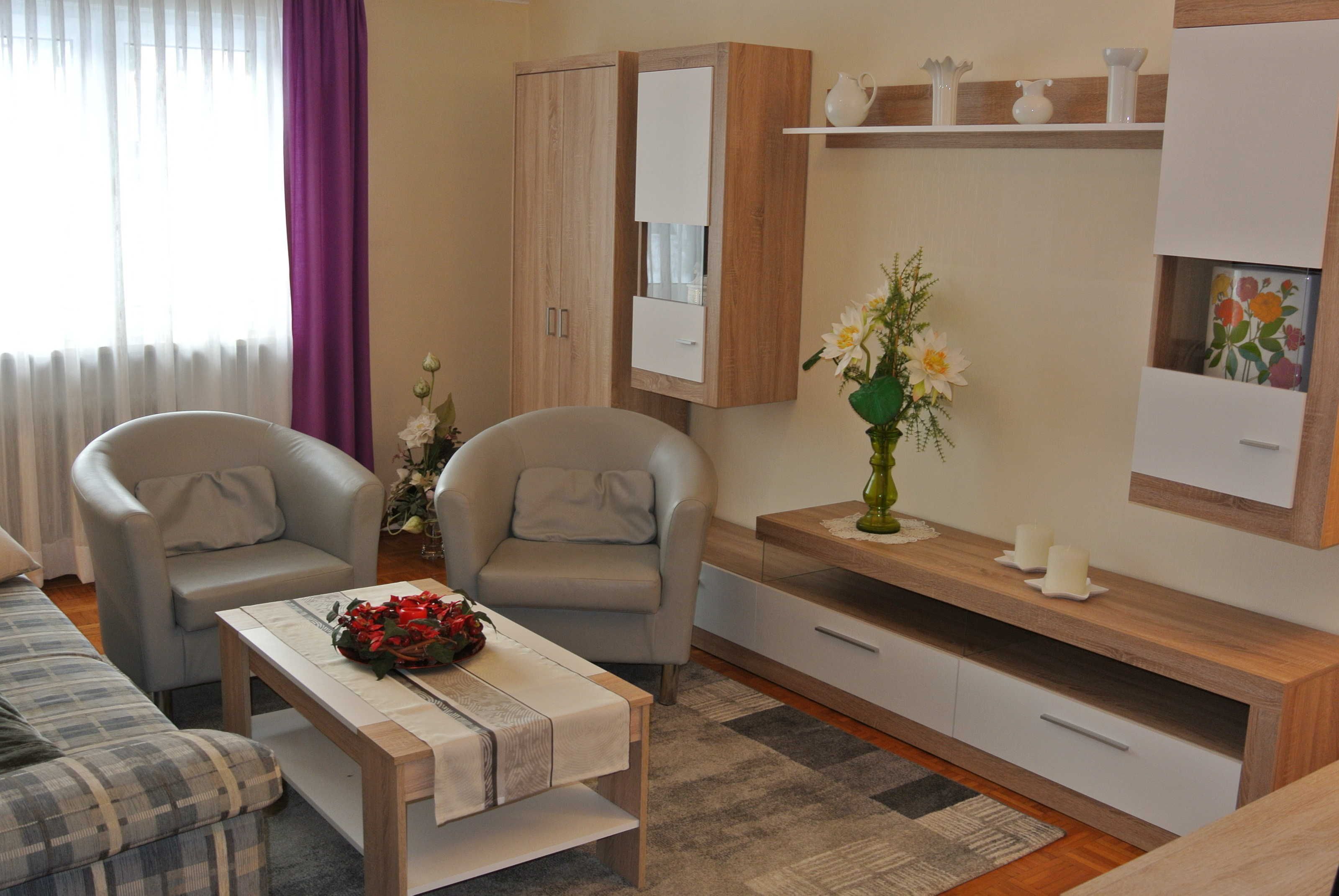 A modern living room with a sofa, two armchairs, a coffee table, a cabinet, and a small side table with a vase of flowers.