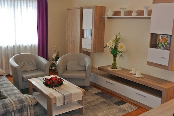 A modern living room with a sofa, two armchairs, a coffee table, a cabinet, and a small side table with a vase of flowers.