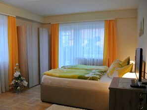 A bedroom with a bed, curtains, a small Christmas tree, and a television.