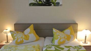 Ein Doppelbett mit Blumenmuster auf der Bettwäsche, zwei Kissen mit gelb-weißer Musterung und ein an der Wand hängendes Bild von Steinen und Pflanzen.