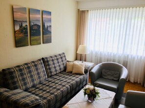 Un salon comprenant un canapé, un fauteuil, une table ornée d’un vase de fleurs et trois tableaux accrochés au mur.
