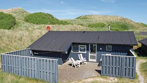 A small, dark-colored cabin with a deck, two lounge chairs, and a small outdoor area. - Nice home in Blokhus with kitchen (Blokhus)