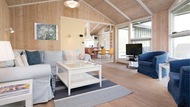 A spacious living room with a wooden ceiling, a white sofa, a blue armchair, and a television. - Nice home in Blokhus with kitchen (Blokhus)