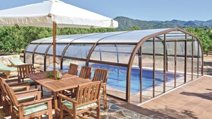 Une serre abritant une piscine, des meubles en bois et un parasol blanc.