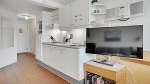 A modern kitchen with white cabinetry, a built-in dishwasher, and a flat-screen TV on a wooden stand. - 1 bedroom gorgeous apartment in Fanø (Fanø)
