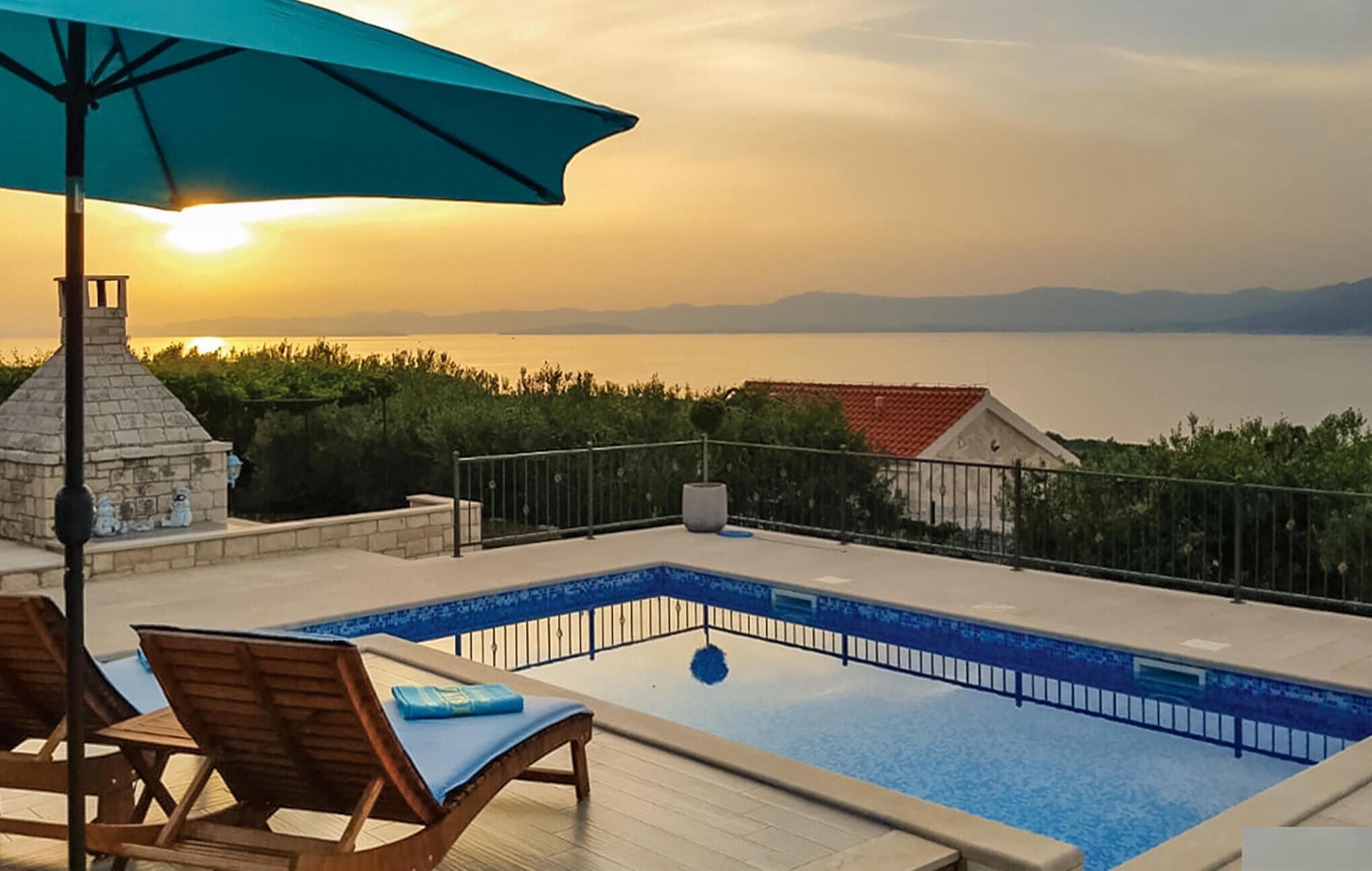 Zona de piscina con vistas al mar y las montañas, una chimenea de piedra y sillones de descanso.