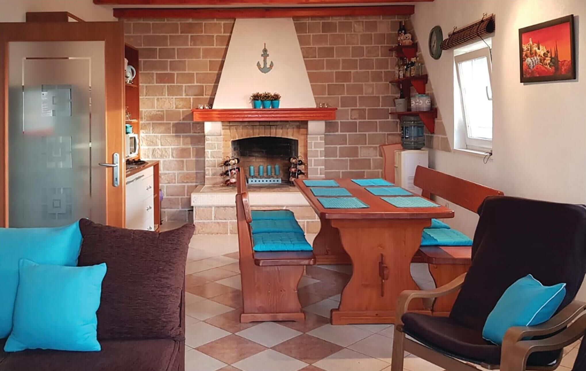 A cozy living room with a fireplace, a dining table with blue placemats, a sofa with blue cushions, and a wooden chair.