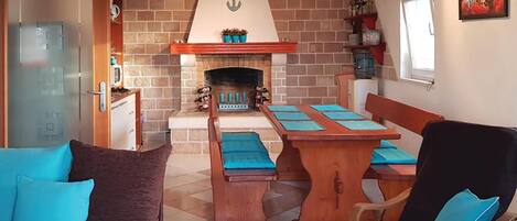 A cozy living room with a fireplace, a dining table with blue placemats, a sofa with blue cushions, and a wooden chair.