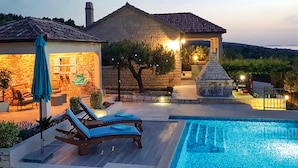 Un espace aménagé au bord de la piscine, avec des chaises longues, un bâtiment en pierre et un coin barbecue.