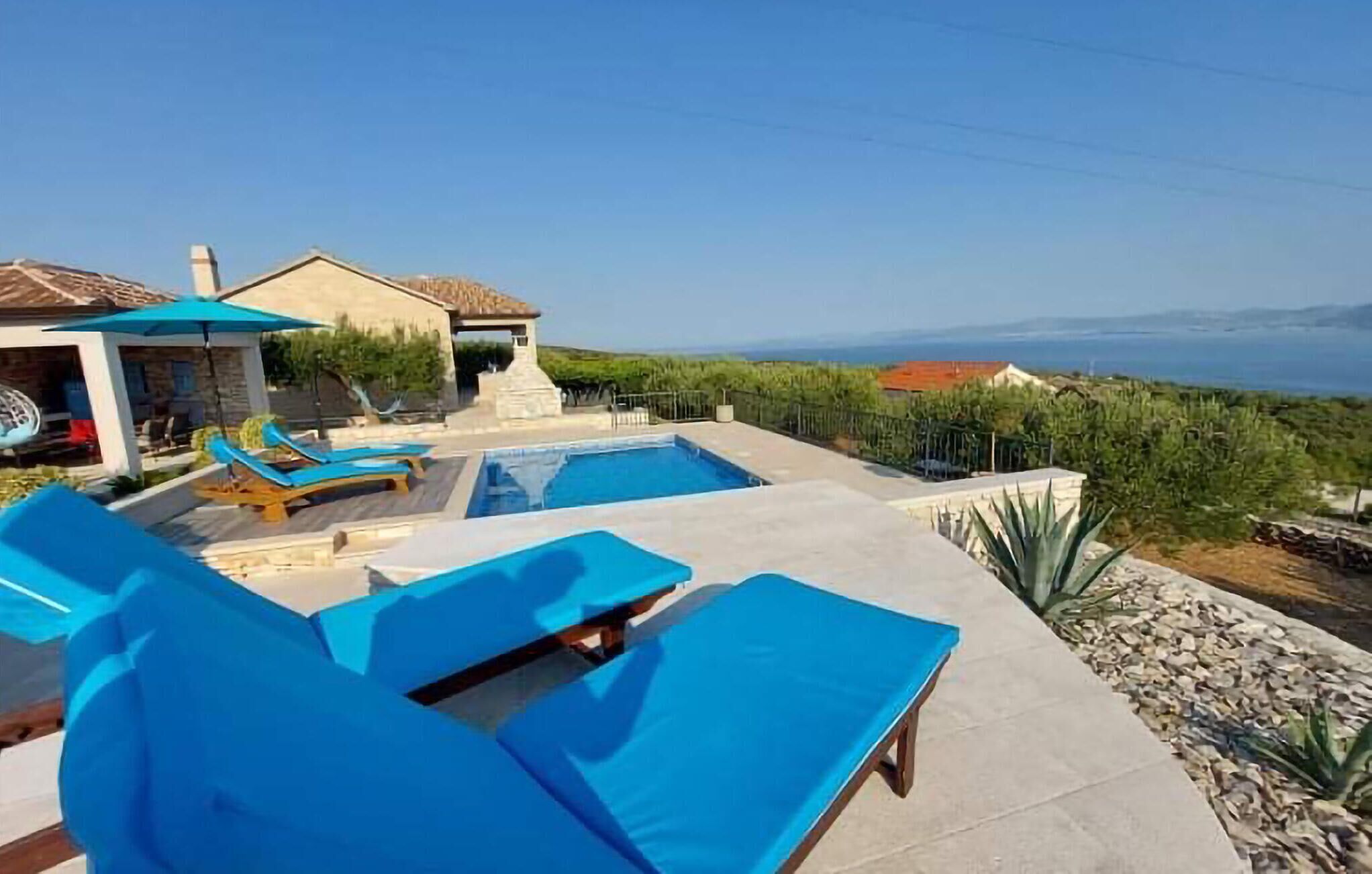 A pool area with blue lounge chairs, a stone building, and a view of the sea.