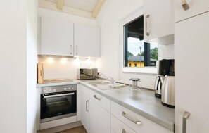 A compact kitchen with white cabinets, a built-in oven, a coffee maker, and a window providing a view of the outside. - Cozy home in Thale with sauna (Thale)