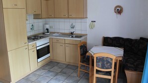 A compact kitchen with wooden cabinets, a stove, and a sink. There is a small dining area with a table and chairs. - Apartment No. 5 - To the little mermaid (Friedrichskoog)