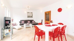 Una sala de estar moderna con un sofá, una mesa de comedor con sillas rojas, un televisor sobre un pedestal de vidrio y un cuadro en la pared.