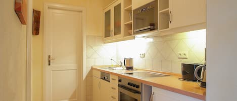 A compact kitchen with white cabinets, a microwave, an oven, and a sink.