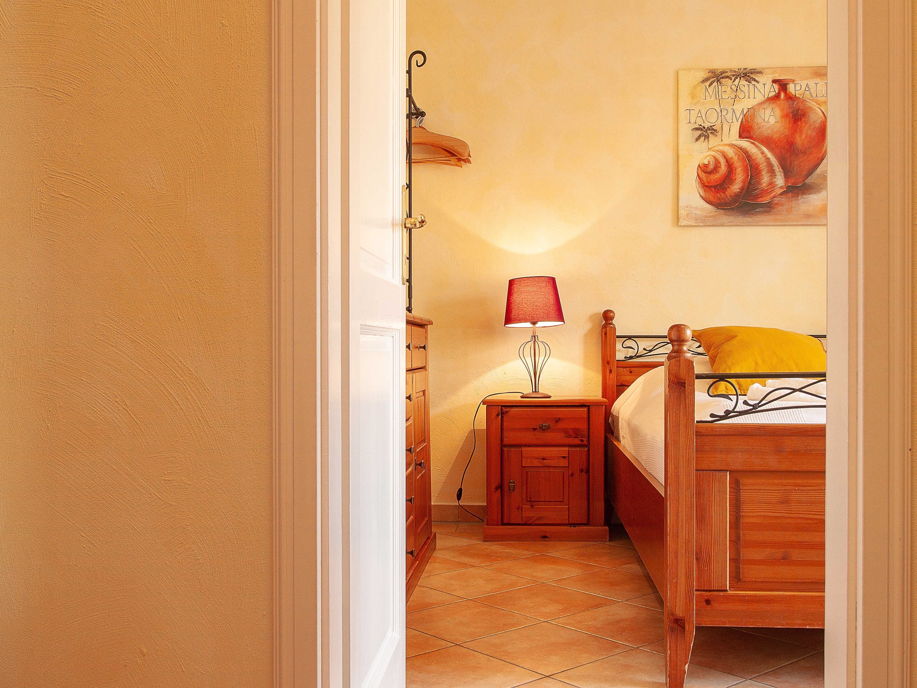 A bedroom with a wooden bed, a nightstand with a lamp, a wooden wardrobe, and a painting on the wall.