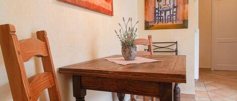 A dining area with a wooden table, chairs, and a red cushioned bench. There is a potted plant on the table.