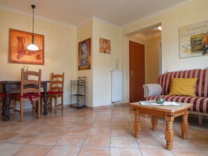 Una zona pranzo con sedie e tavolo in legno, un soggiorno con divano e tavolino, e un corridoio con una porta.