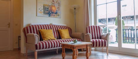 Un salon avec un canapé à rayures, une table basse en bois et une grande fenêtre donnant sur des immeubles.