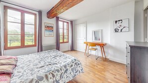 A bedroom with a bed, a desk, a chair, a dresser, and large windows. - Appartement jolie vue rivière (Jaulgonne)