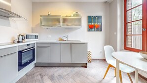 A modern kitchen with a microwave, kettle, and oven, a sink with a faucet, and a dining area with a table and chairs. - Appartement jolie vue rivière (Jaulgonne)