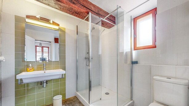 Ein Badezimmer mit einer Duschkabine, einem Waschbecken mit Spiegel und einer Toilette.