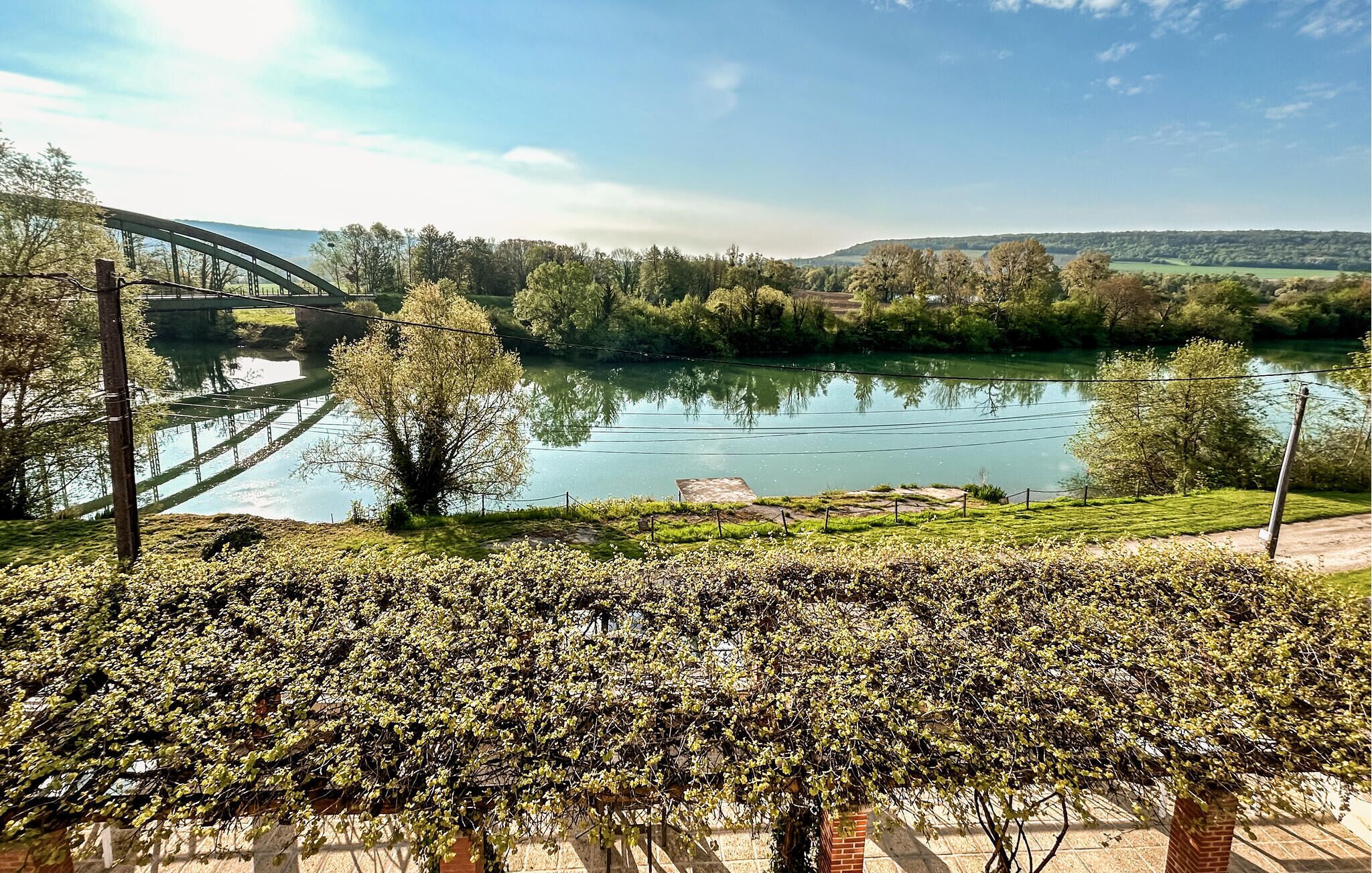 Un riu amb un pont, vegetació exuberant i un cel serè.