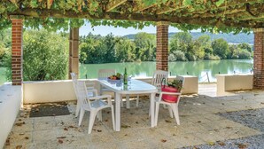 A covered outdoor seating area with a table and chairs, overlooking a lake and surrounded by greenery. - Appartement jolie vue rivière (Jaulgonne)