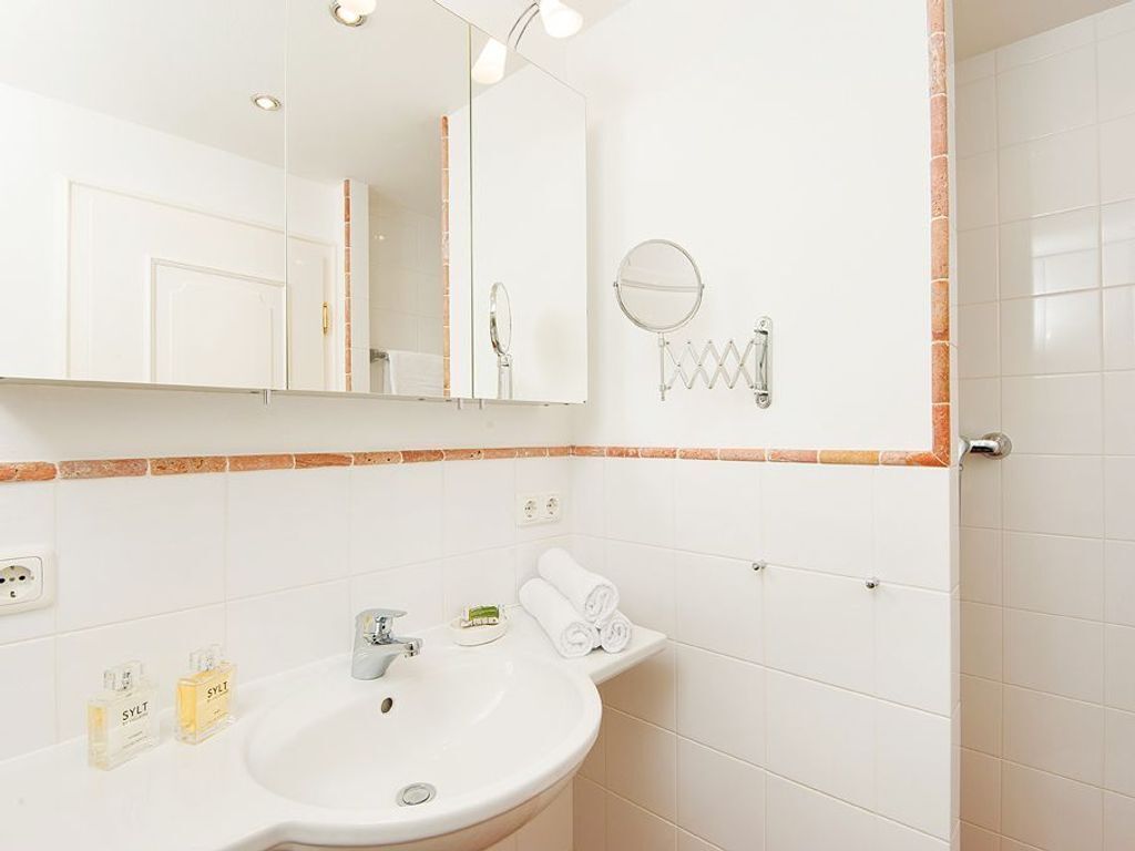 A bathroom with a white sink, mirror, and towel rack. There are toiletries on the sink and a towel rack with towels.