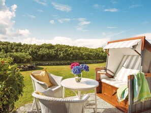 Un espace extérieur aménagé avec des meubles en osier, comprenant une table et des chaises, un banc rembourré et une vue sur un vignoble.