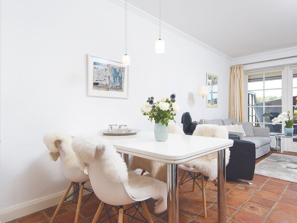 Un espace repas moderne avec une table blanche, des fauteuils moelleux et un vase rempli de fleurs.