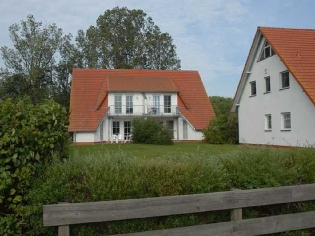 A two-story house with a red roof and white walls, surrounded by greenery.