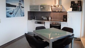 A modern kitchen with a glass-top table, black chairs, a stainless steel range hood, and a microwave. - (244) 2-room apartment - apartment complex holiday dreams (Kühlungsborn)