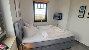 A bedroom with a bed, a window, a TV, and a bedside table. - (244) 2-room apartment - apartment complex holiday dreams (Kühlungsborn)