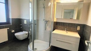 A modern bathroom with a glass-enclosed shower, a toilet, and a vanity with a mirror. - (244) 2-room apartment - apartment complex holiday dreams (Kühlungsborn)