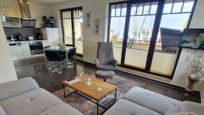 A modern living room with a sofa, a coffee table, and a dining area with a chair and table. - (244) 2-room apartment - apartment complex holiday dreams (Kühlungsborn)